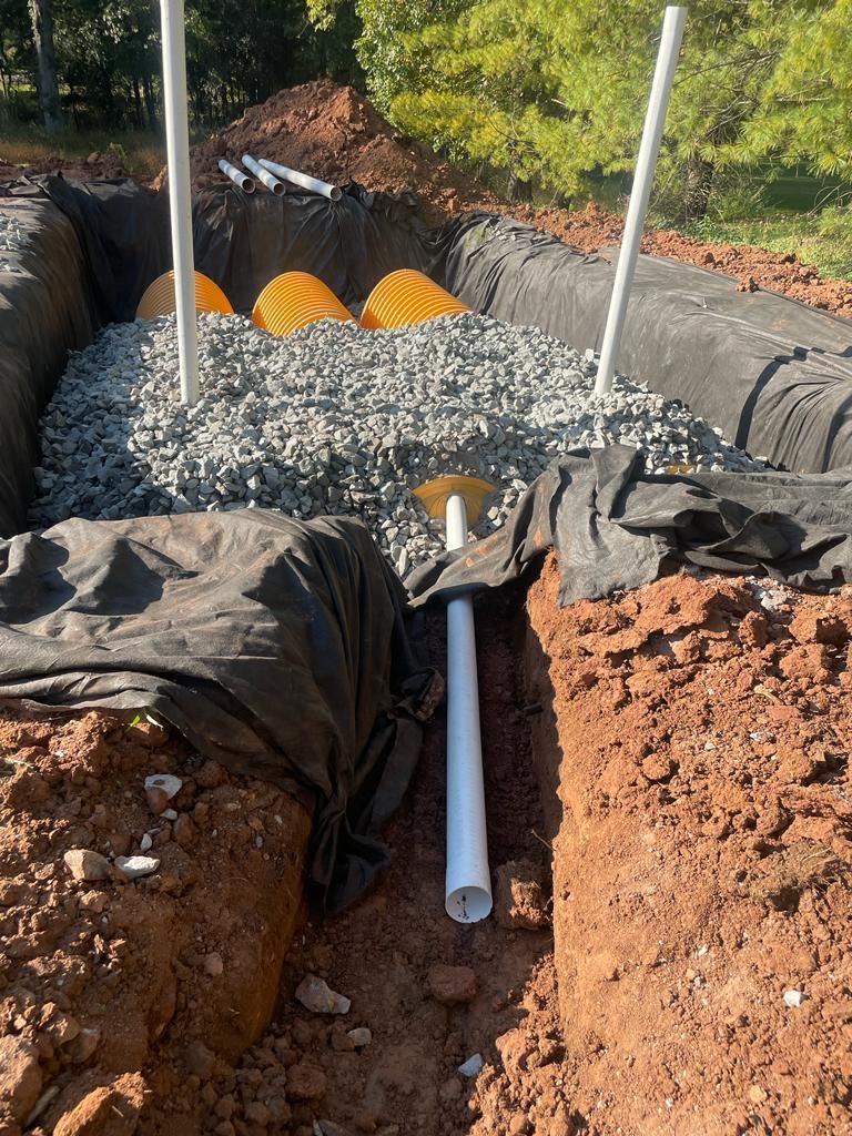 A pipe is laying in the dirt next to a pile of gravel.