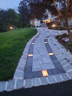 A walkway with lights on the side of it leading to a house.