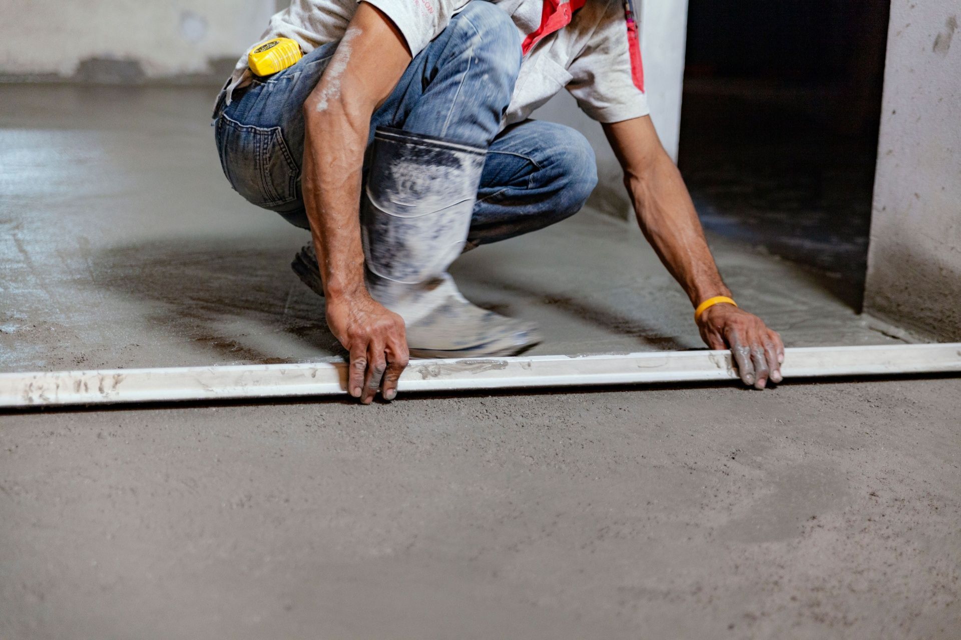 A man is kneeling down on the floor using a level.