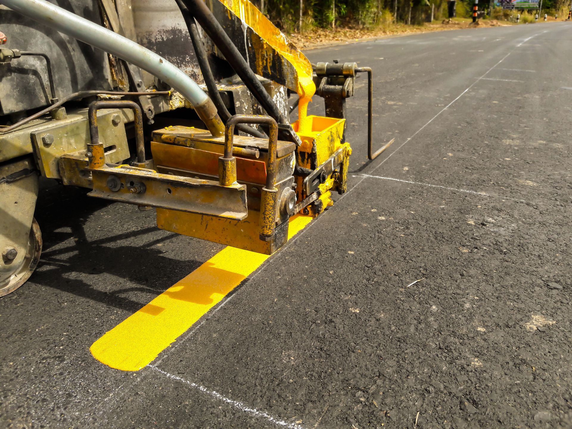 A yellow machine is painting a yellow line on the road