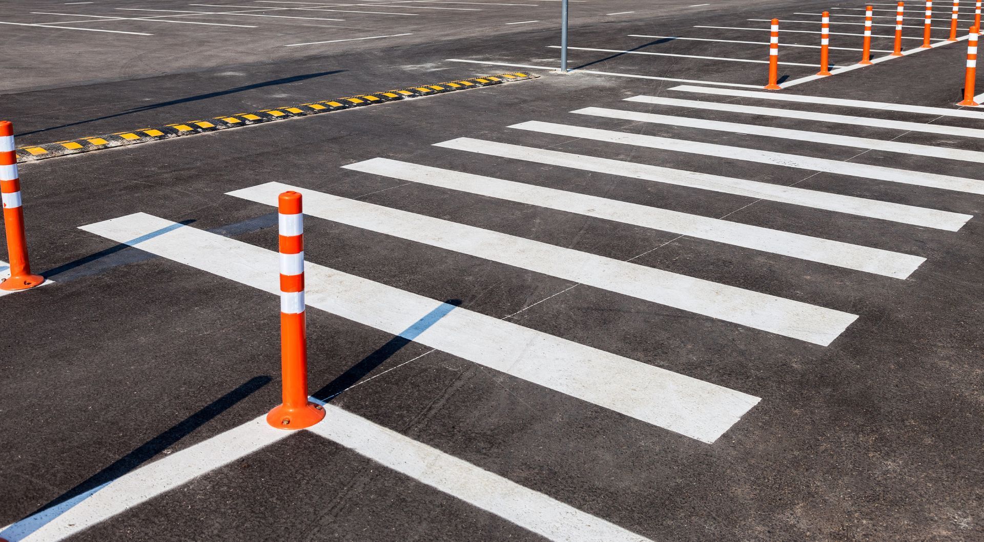 A crosswalk with orange poles and white stripes on the road.