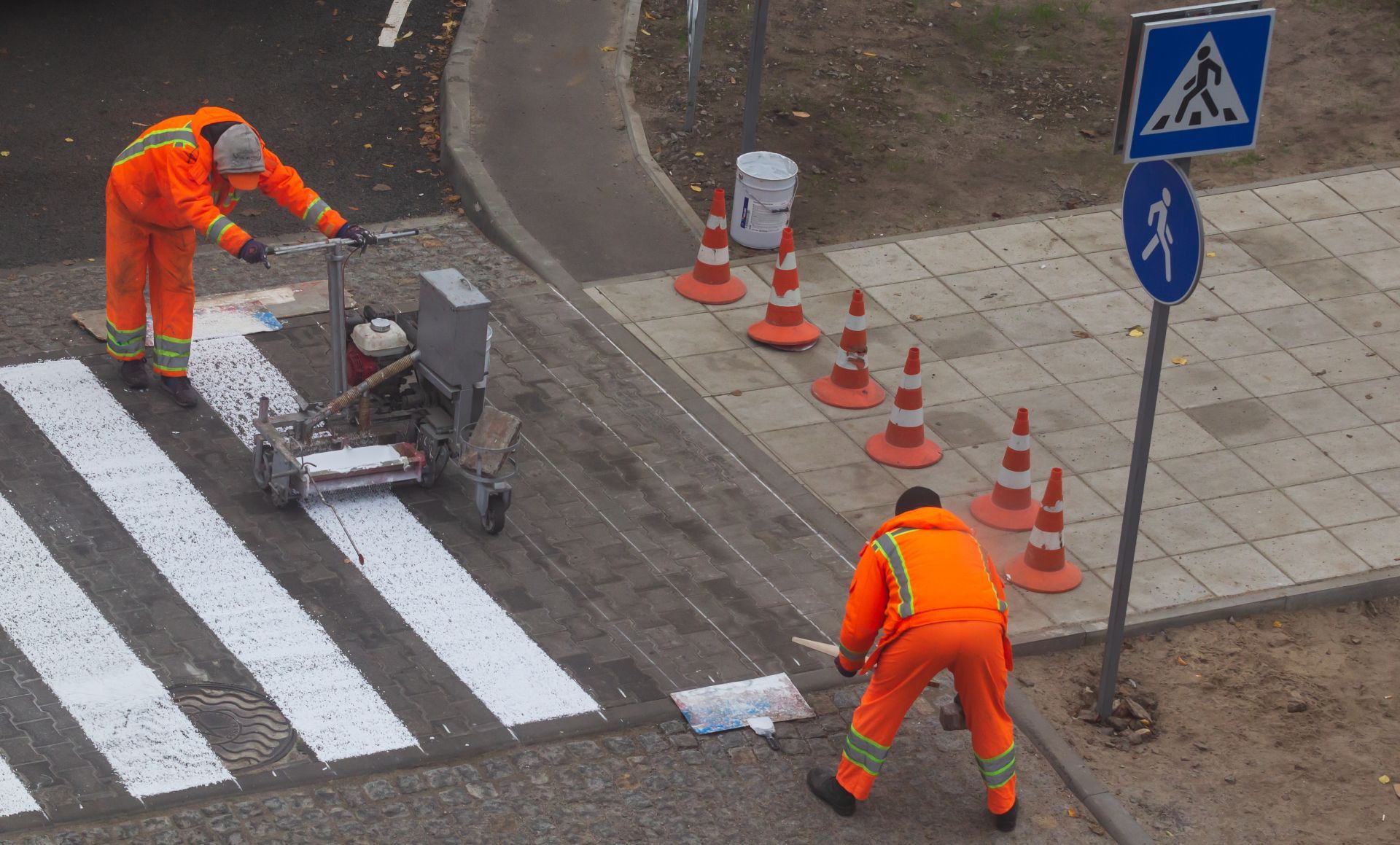 Two men are painting a crosswalk on a street