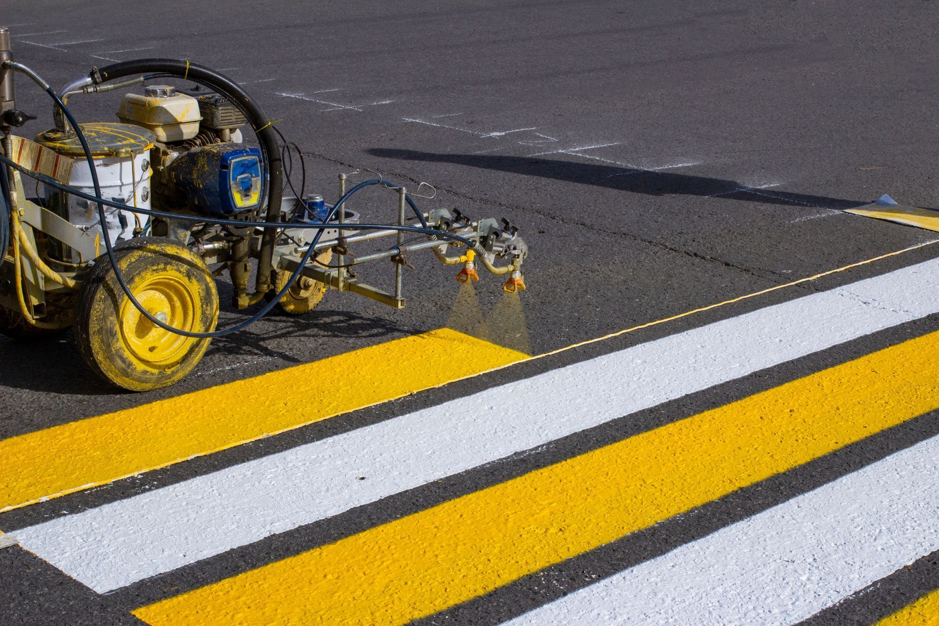 A machine is painting yellow and white stripes on a crosswalk.