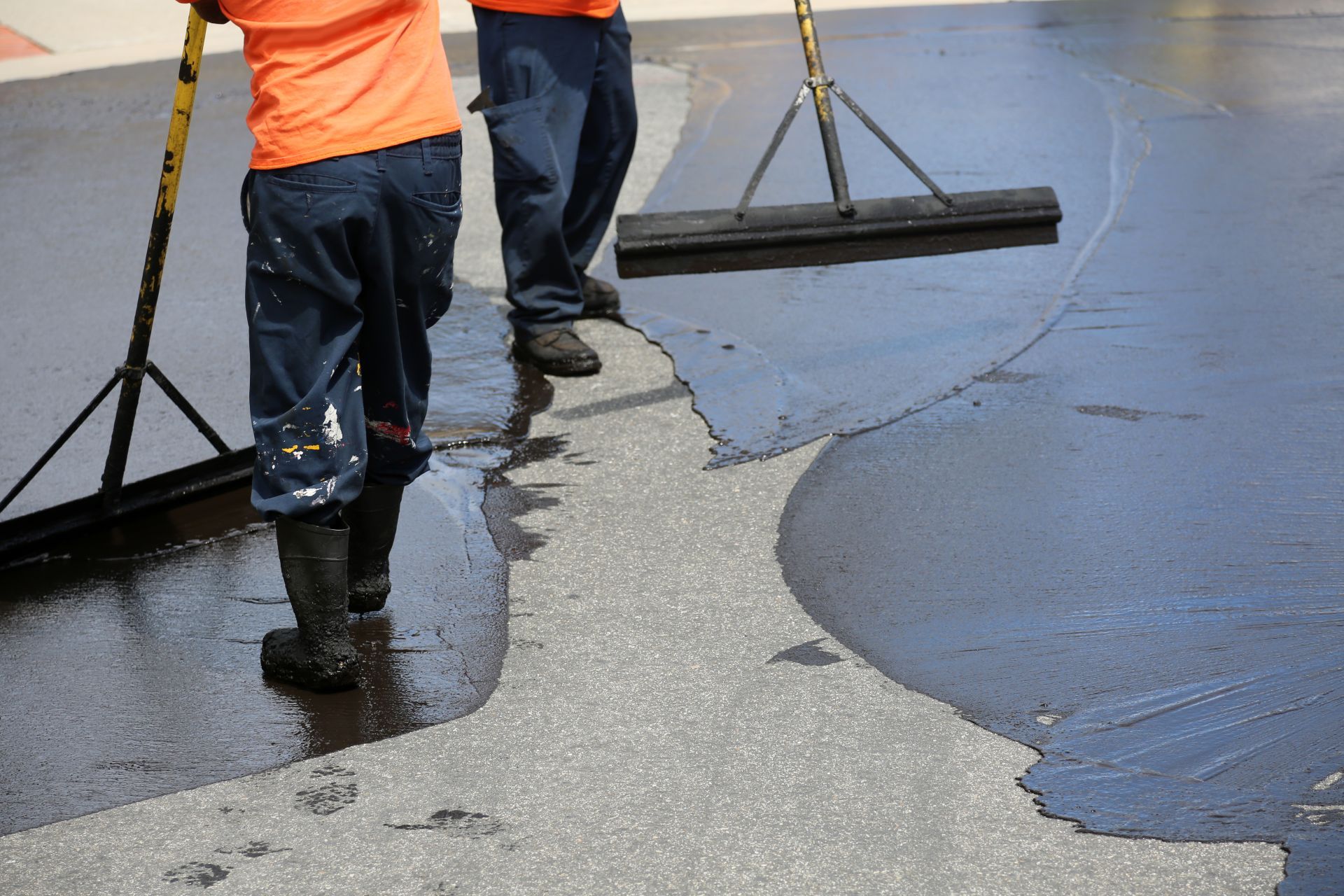 Two men are spreading asphalt on a road with a broom.