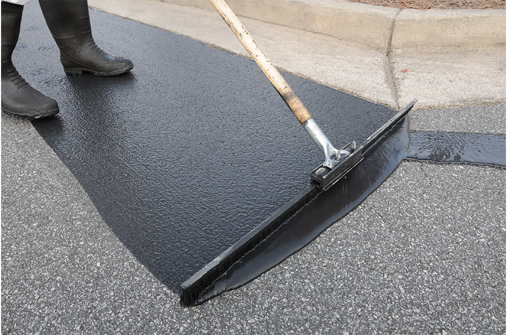 A person is using a rake to spread asphalt on the ground.