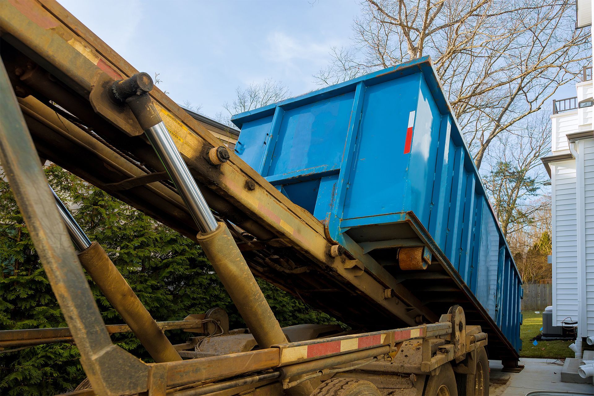 Blue dumpster being lifted onto a truck by a hydraulic arm outdoors
