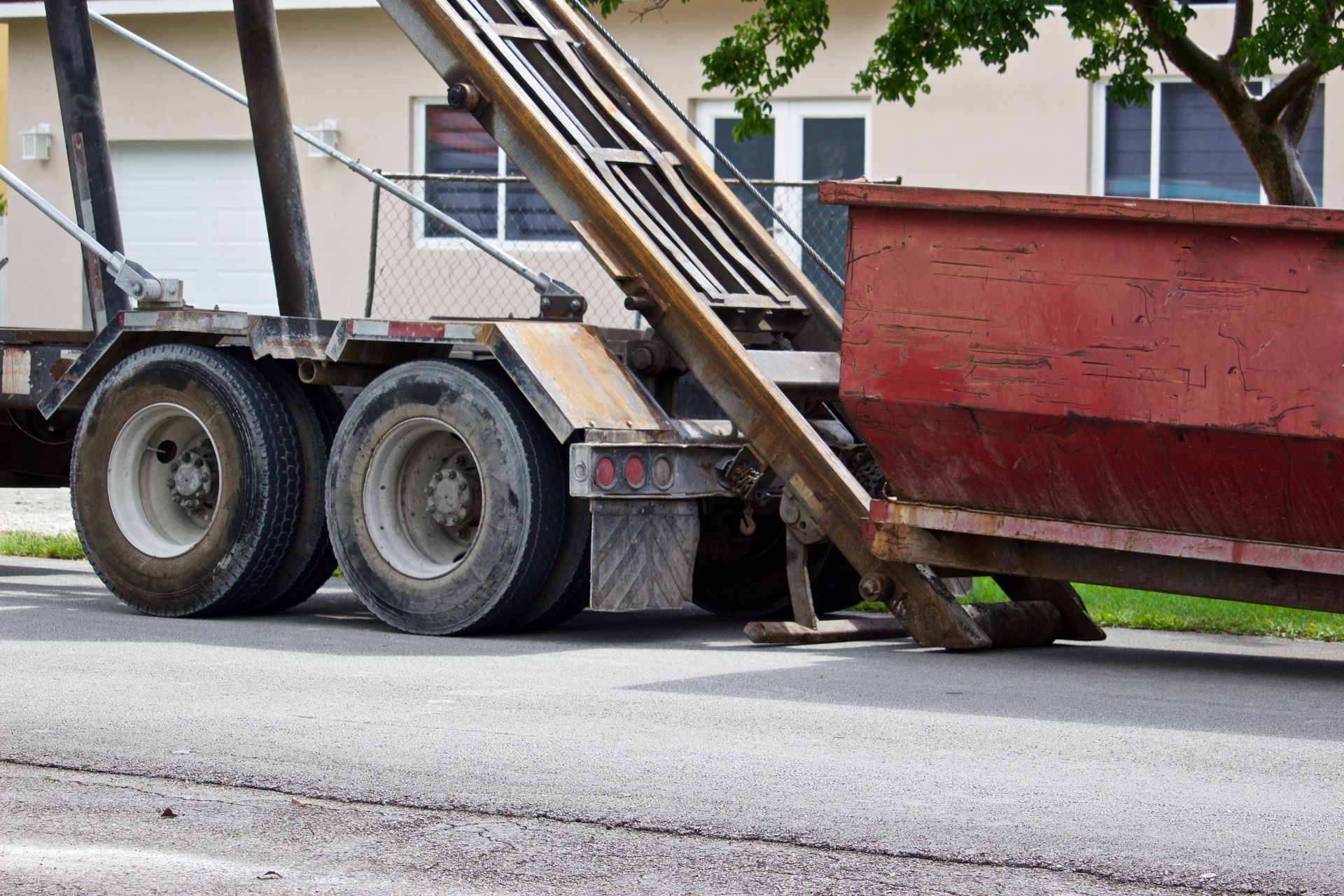 Dump trailer lowering a red bed onto a street from a truck, with wheels and metal ramps visible.