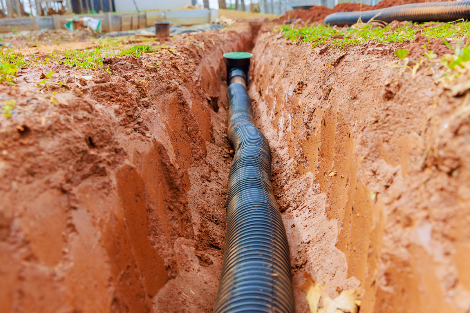 A black pipe is being installed in a trench of dirt.