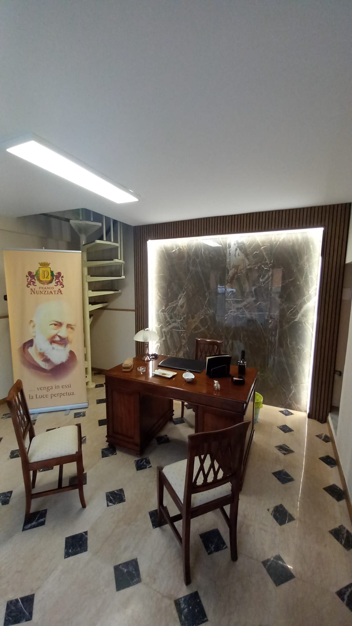 Una stanza con una scrivania, sedie e un cartello sul muro.