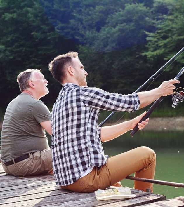 Two men are sitting on a dock fishing in a lake.