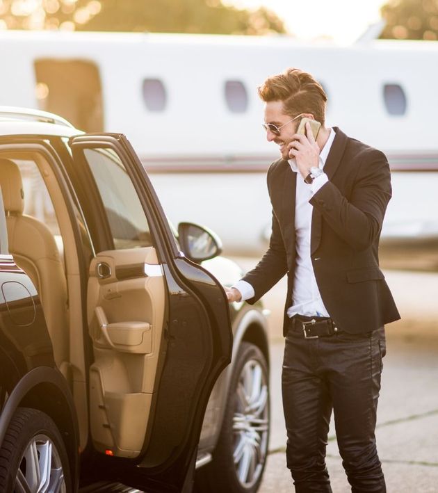 A man is talking on a cell phone while standing next to a car