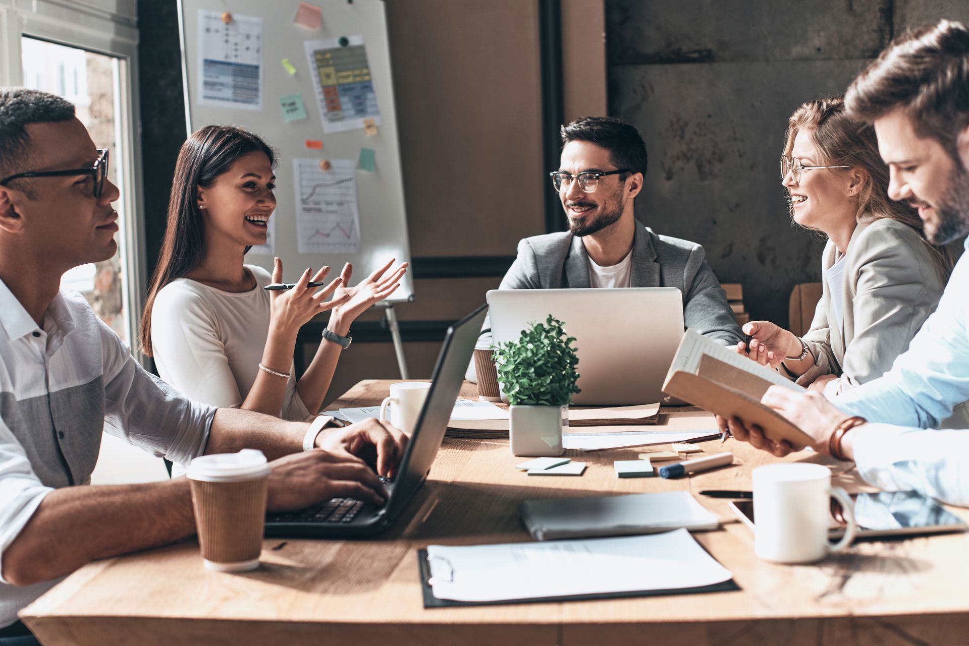 Team meeting around a laptop in a bright office, with notes, coffee cups, and engaged discussion.