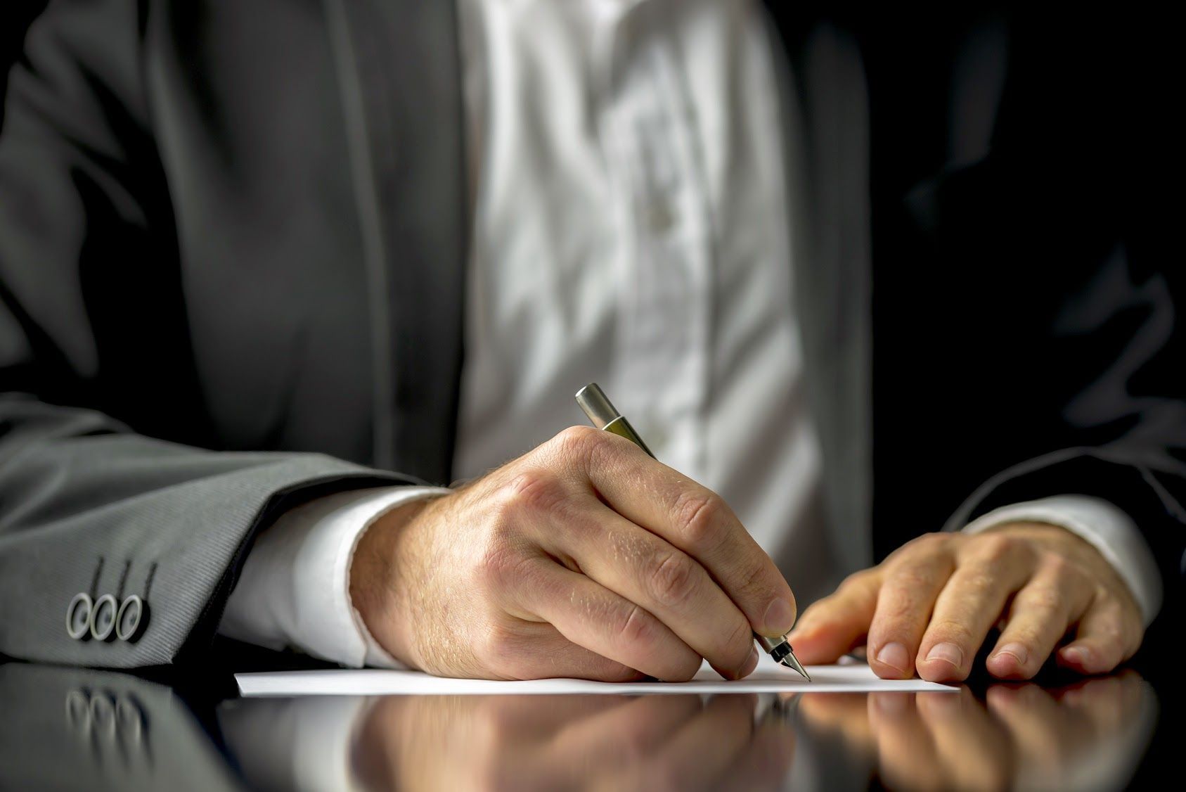 Person in a suit signing a document at a desk with a pen