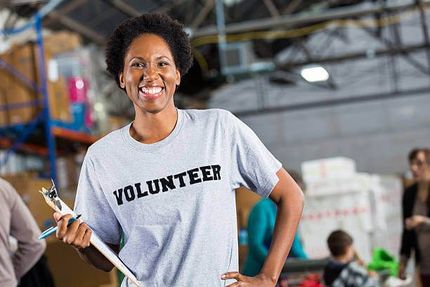 a woman in a volunteer shirt is holding a clipboard and smiling .