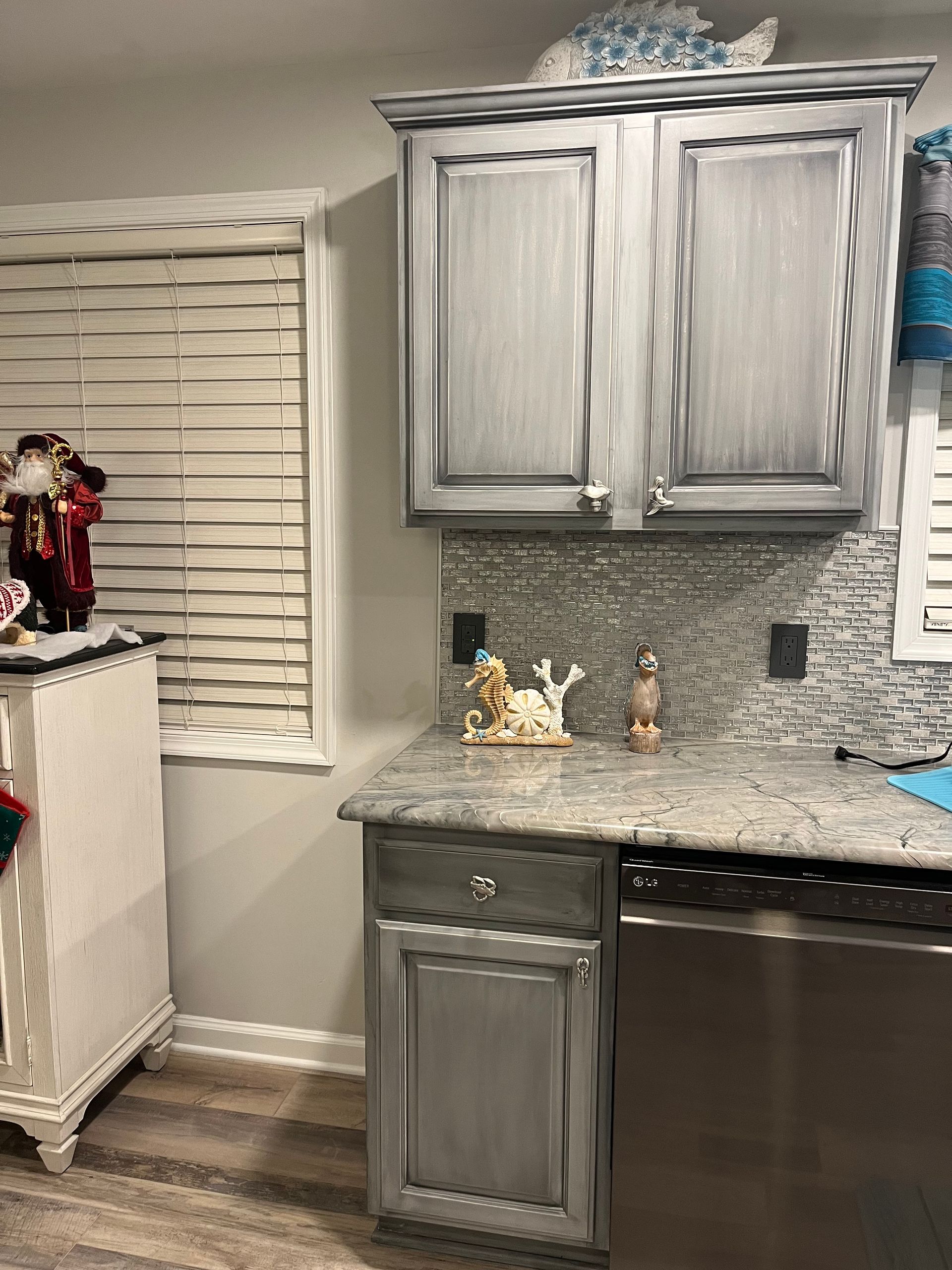 A kitchen with gray cabinets , granite counter tops , and a stainless steel dishwasher.