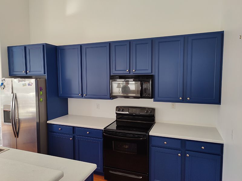 A kitchen with blue cabinets , black appliances , and white counter tops.