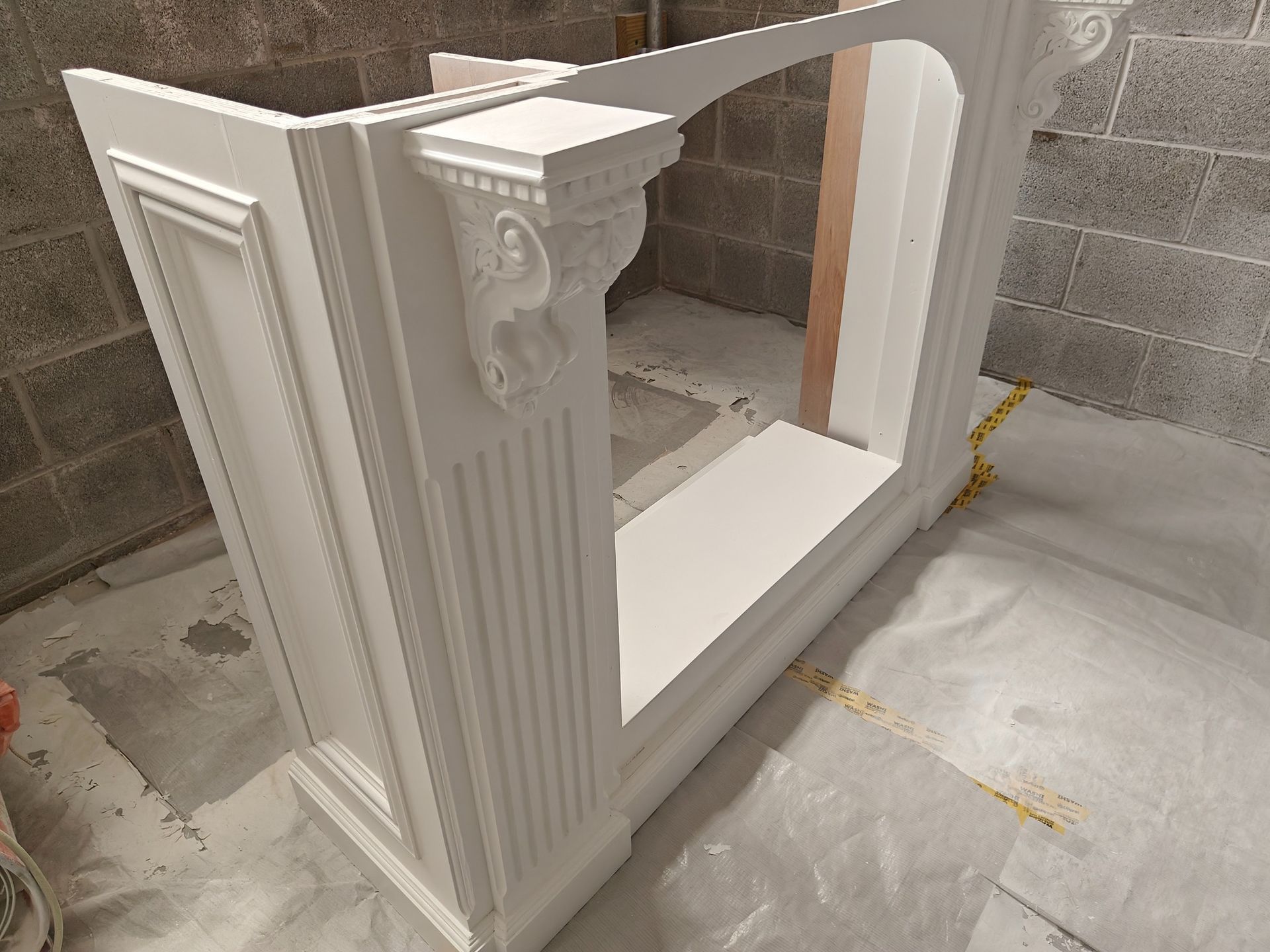 A white fireplace is being painted in a room with a brick wall.