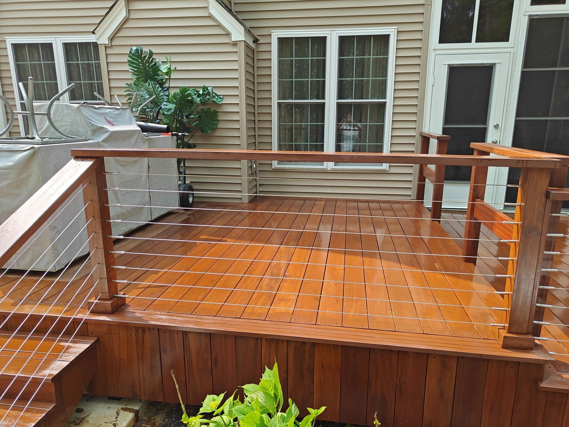 A wooden deck with a wire railing and stairs in front of a house.