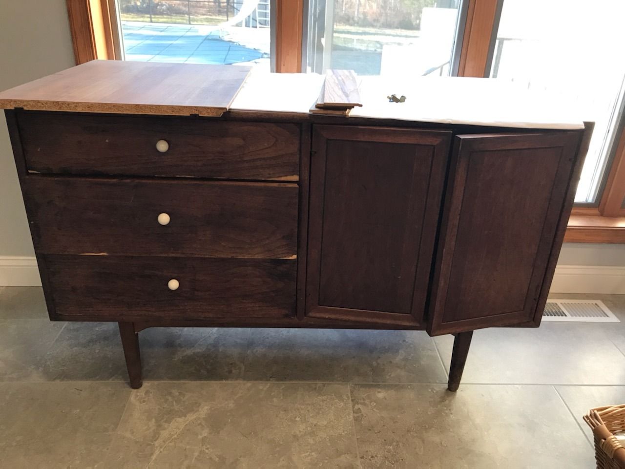 A wooden dresser is sitting on a tiled floor in front of a window.