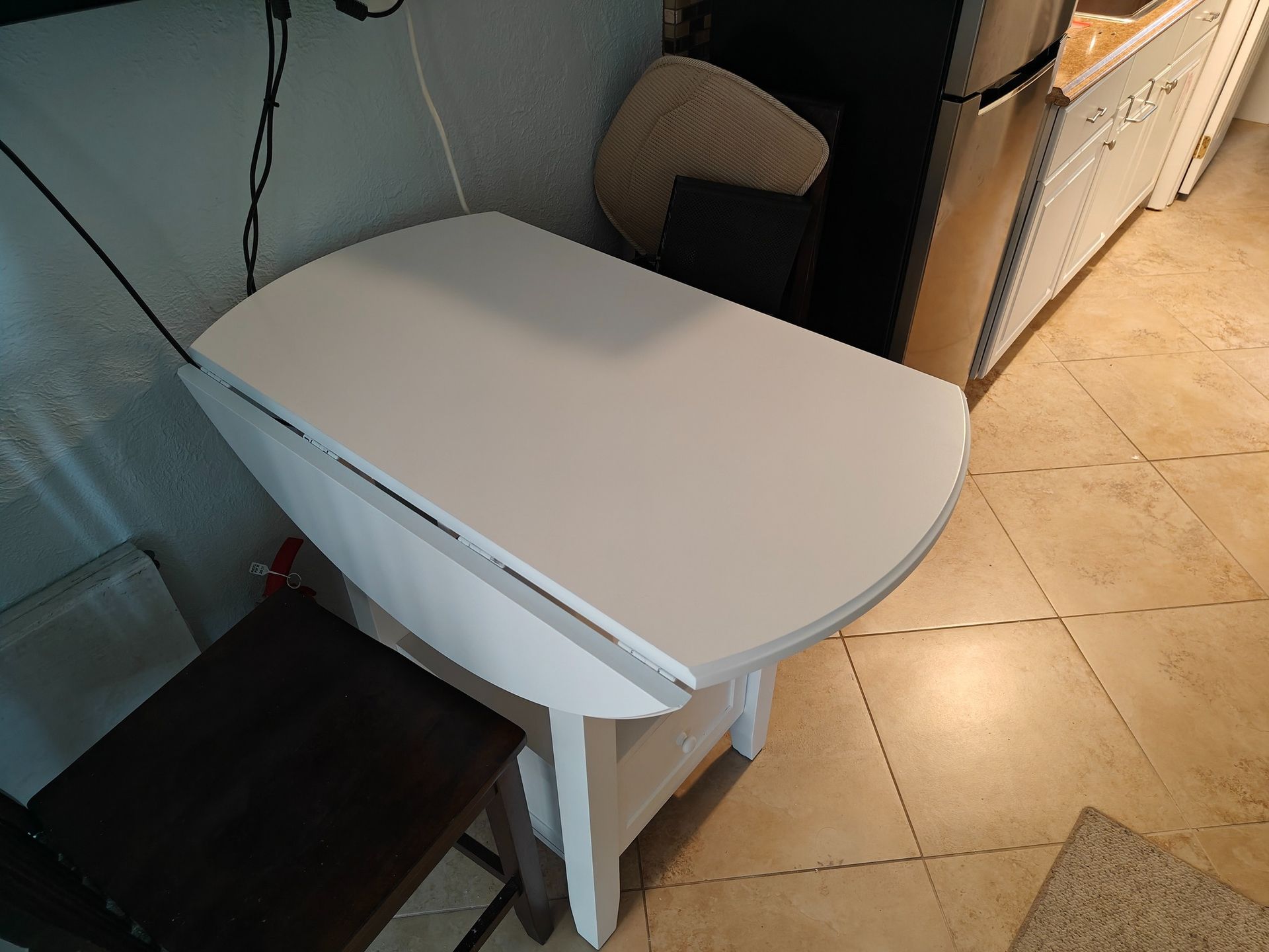 A small white table is sitting in a kitchen next to a chair.
