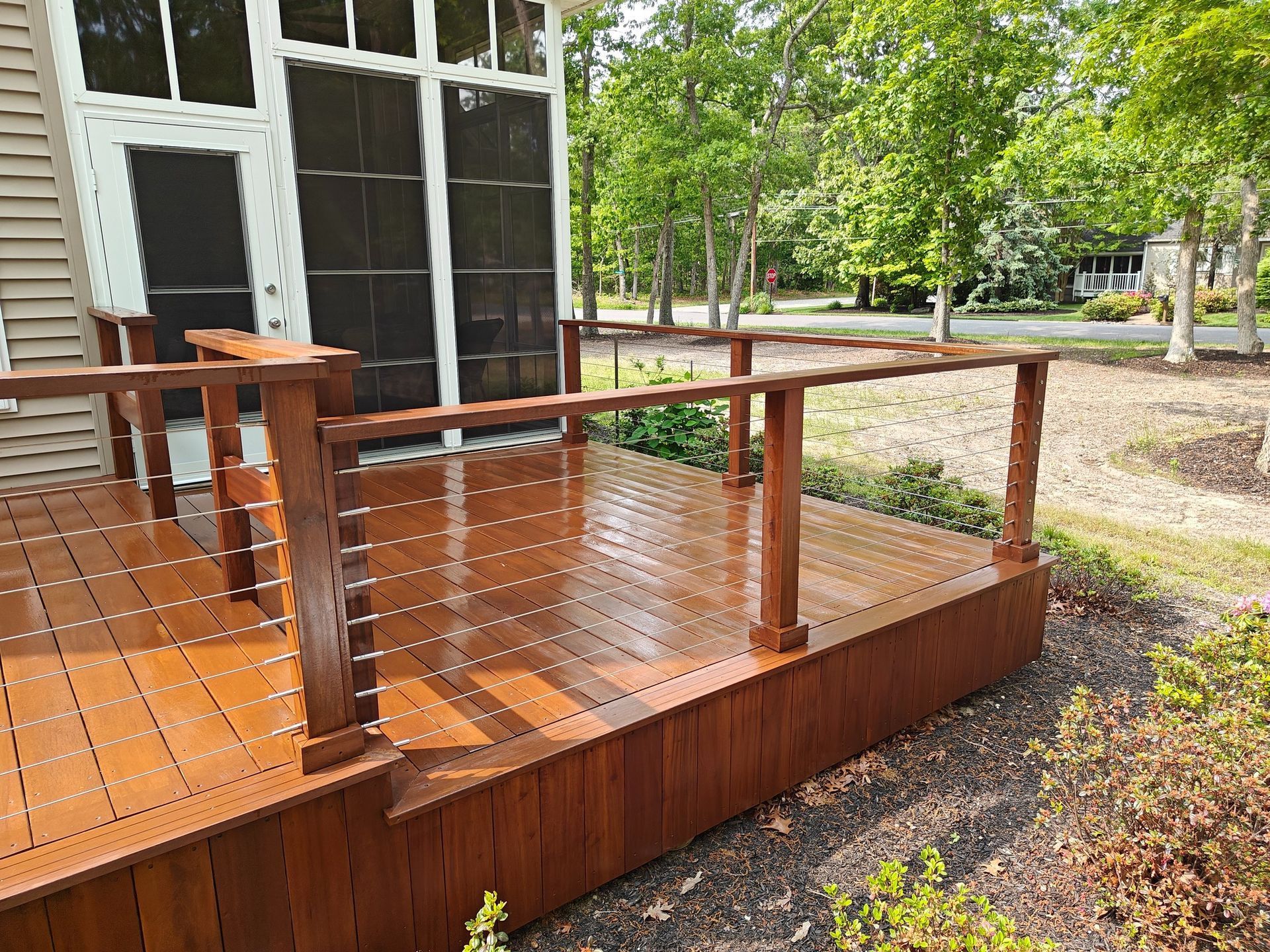 A wooden deck with a wire railing is in front of a screened in porch.