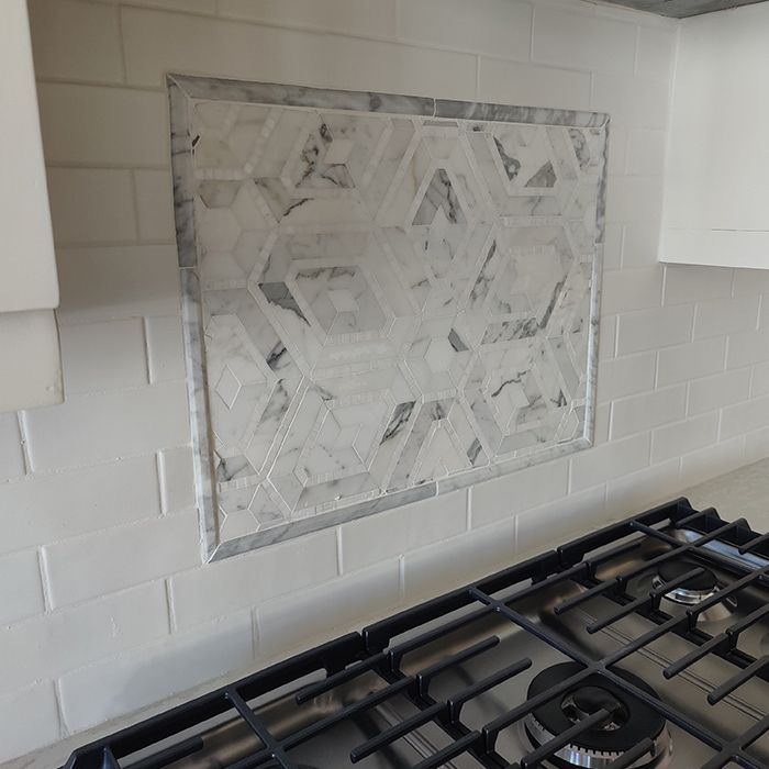A stove top oven in a kitchen with a tiled wall behind it.