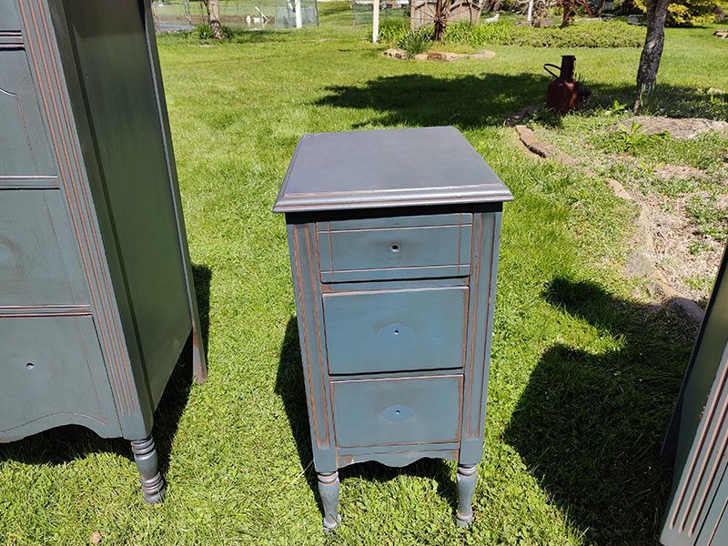 A small blue dresser is sitting on top of a lush green field.