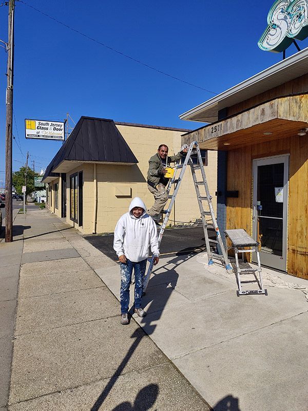 A man is standing on a sidewalk next to a man on a ladder.