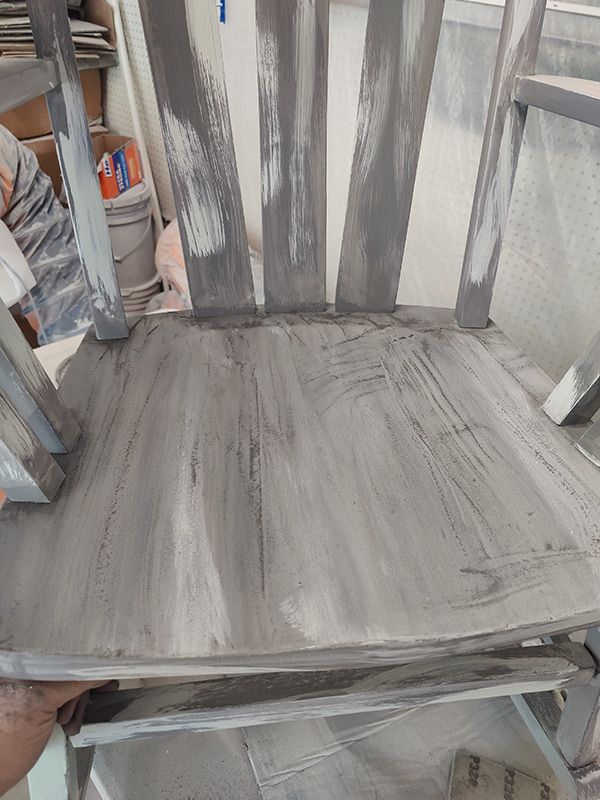 A person is holding a wooden chair that has been painted gray.