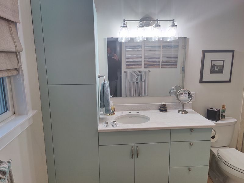 A bathroom with a sink , toilet , mirror and cabinets.