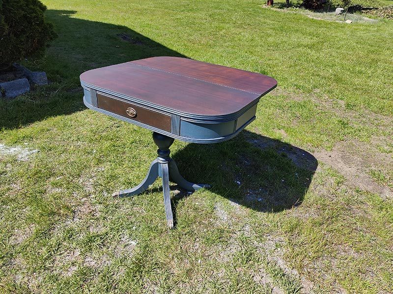 A small table with a drawer is sitting on top of a lush green field.