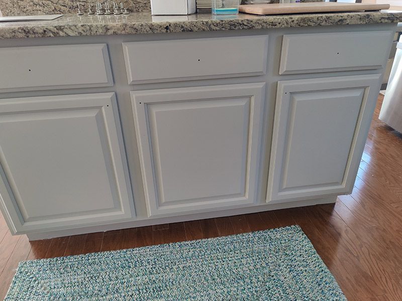 A kitchen counter with white cabinets and a rug on the floor.