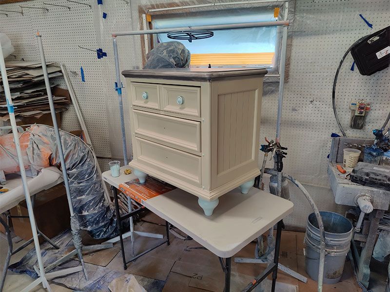 A small white dresser is sitting on top of a white table in a messy room.