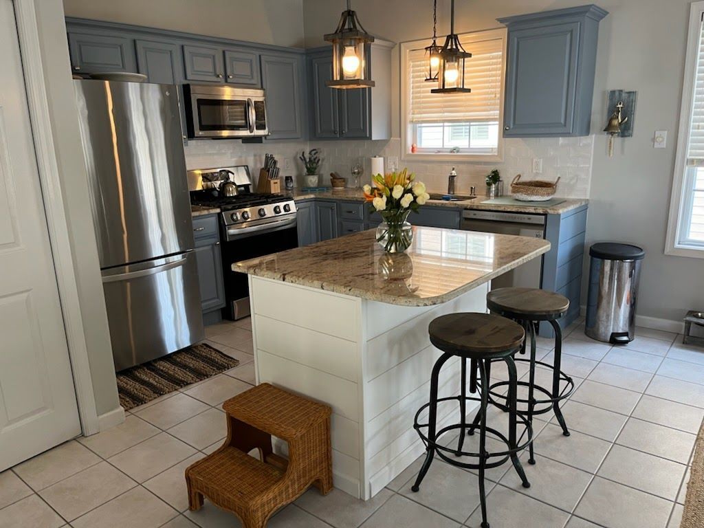A kitchen with blue cabinets , stainless steel appliances , granite counter tops and a large island.