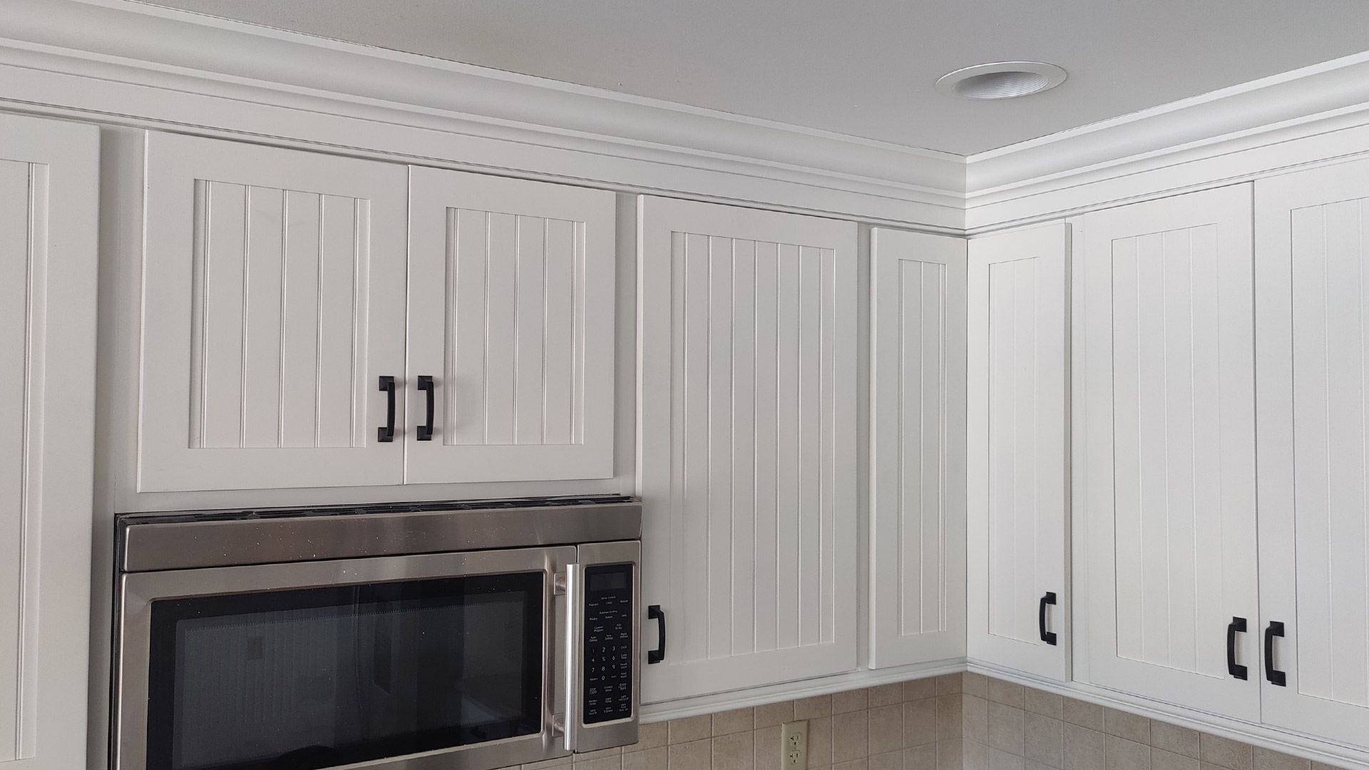 A kitchen with white cabinets and a stainless steel microwave oven.