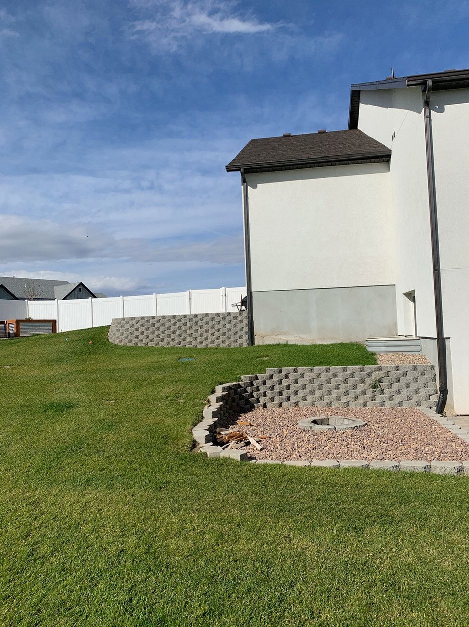 The backyard of a house with a white fence and a dog laying in the grass.