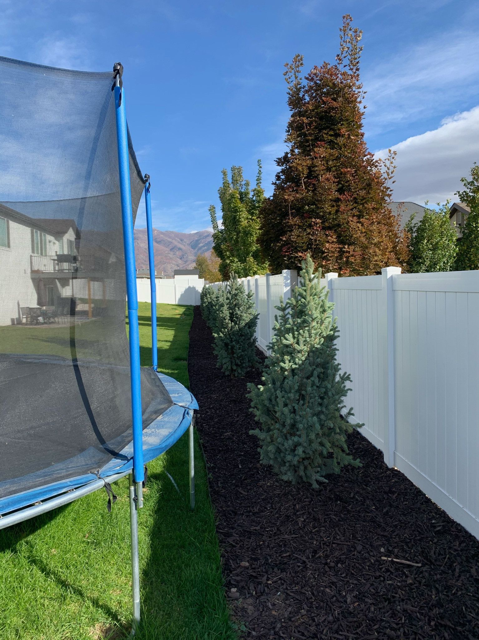 A trampoline is sitting in the grass next to a white fence