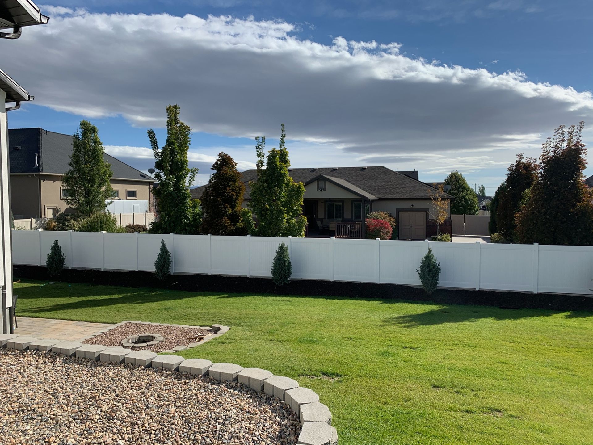 A backyard with a white fence and a house in the background