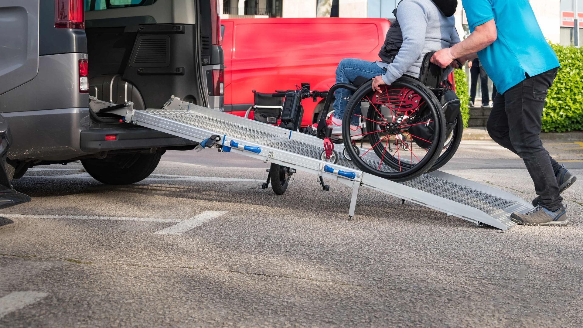 Person in wheelchair being loaded into a van using a portable ramp with help from another person.