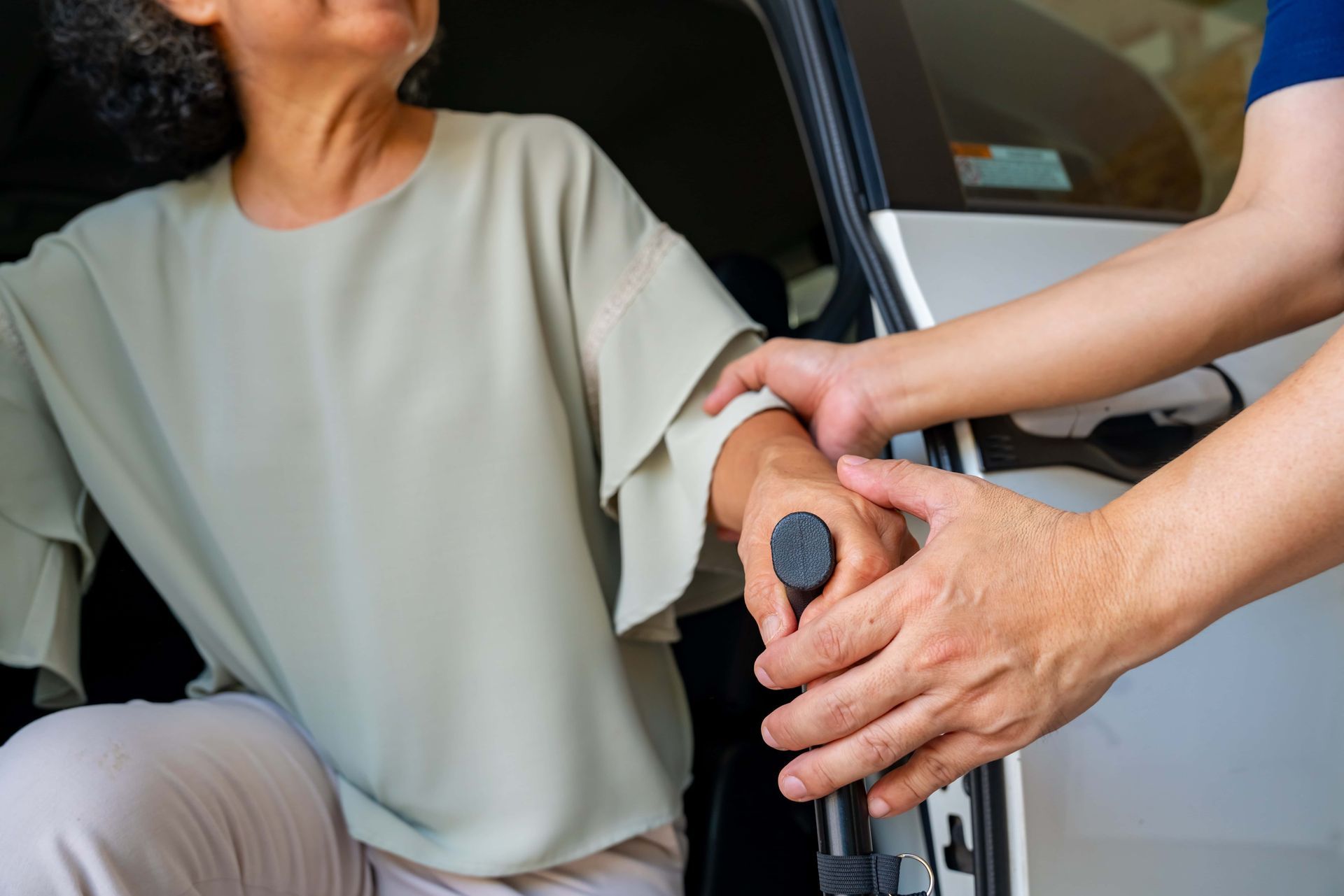 Person helping another into a car from a wheelchair, with a hand on the wheelchair handle