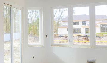 An empty room with a lot of windows and a house in the background.