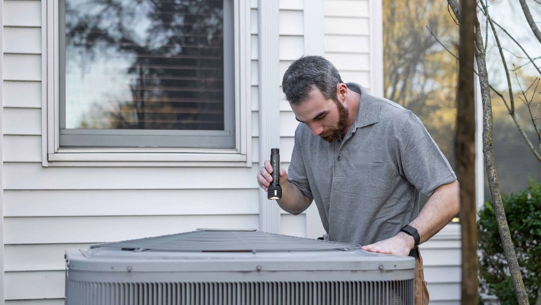 A man is working on an air conditioner outside of a house.