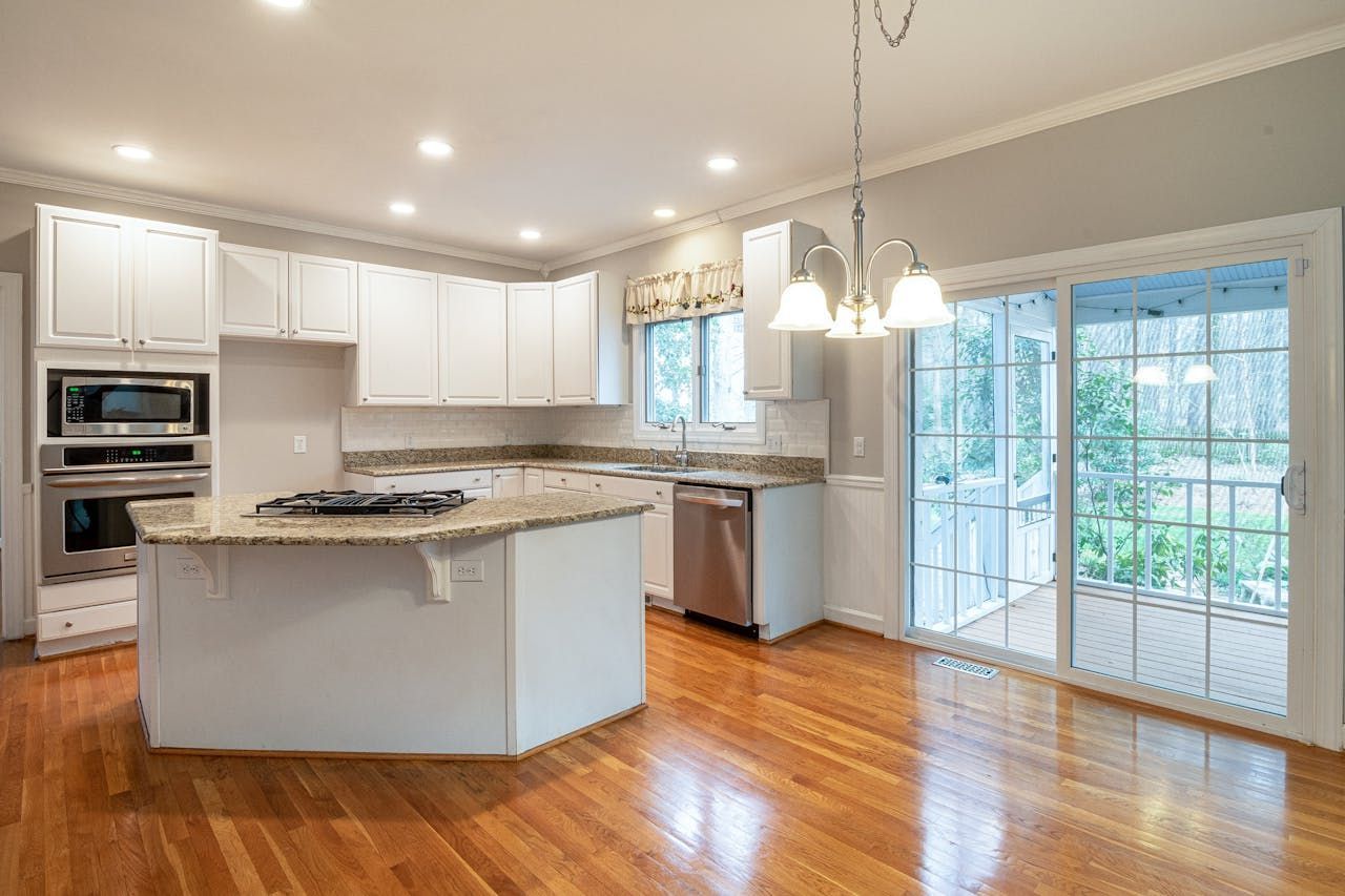 An empty kitchen with hardwood floors , white cabinets , stainless steel appliances and a large island.