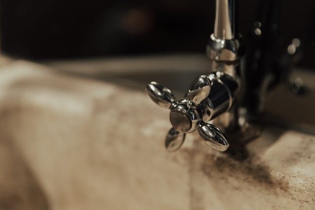 A close up of a faucet with a cross handle on a sink.