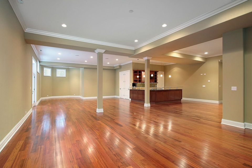 An empty basement with hardwood floors and a kitchen.