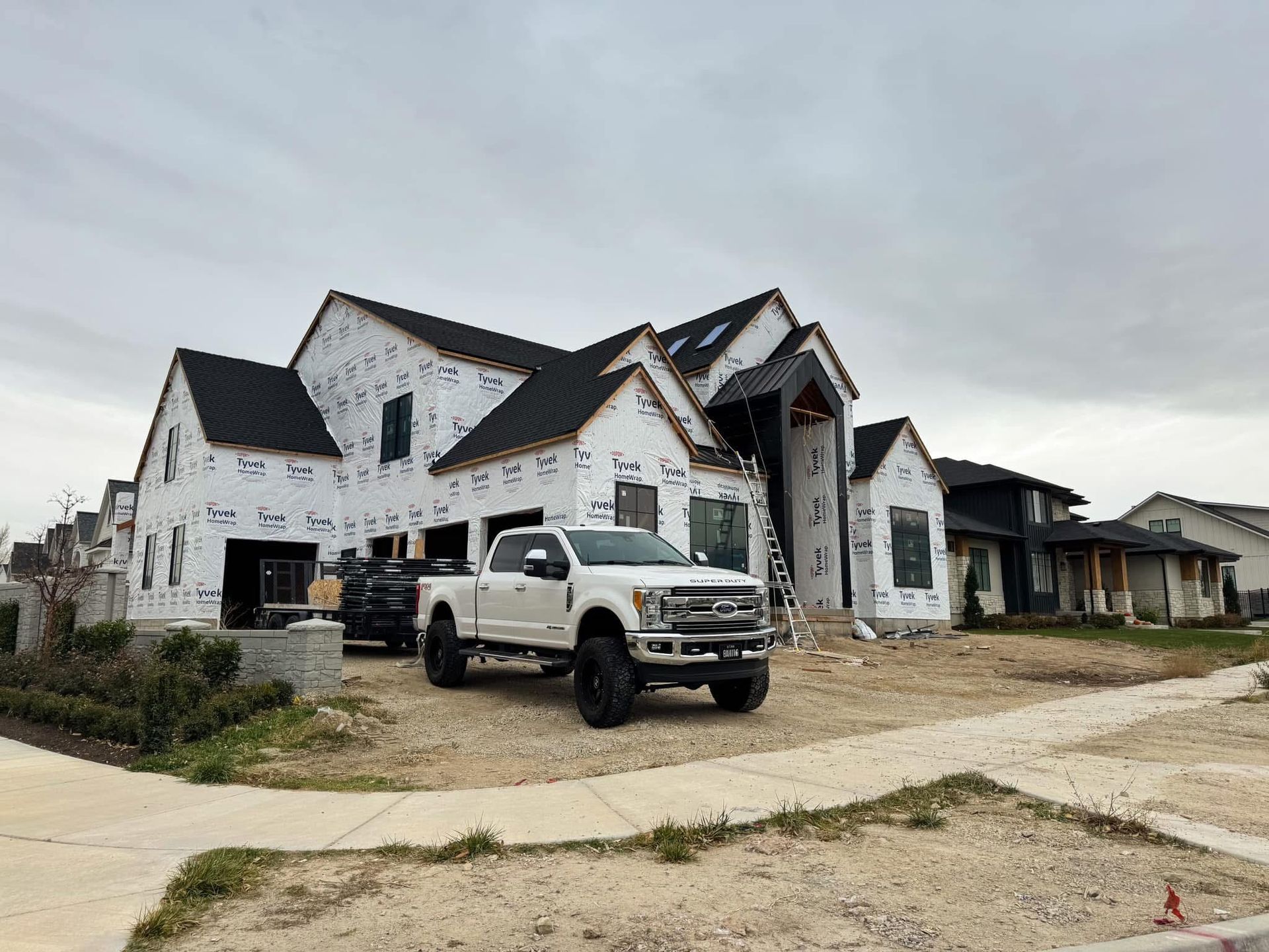 A white truck is parked in front of a large house under construction.