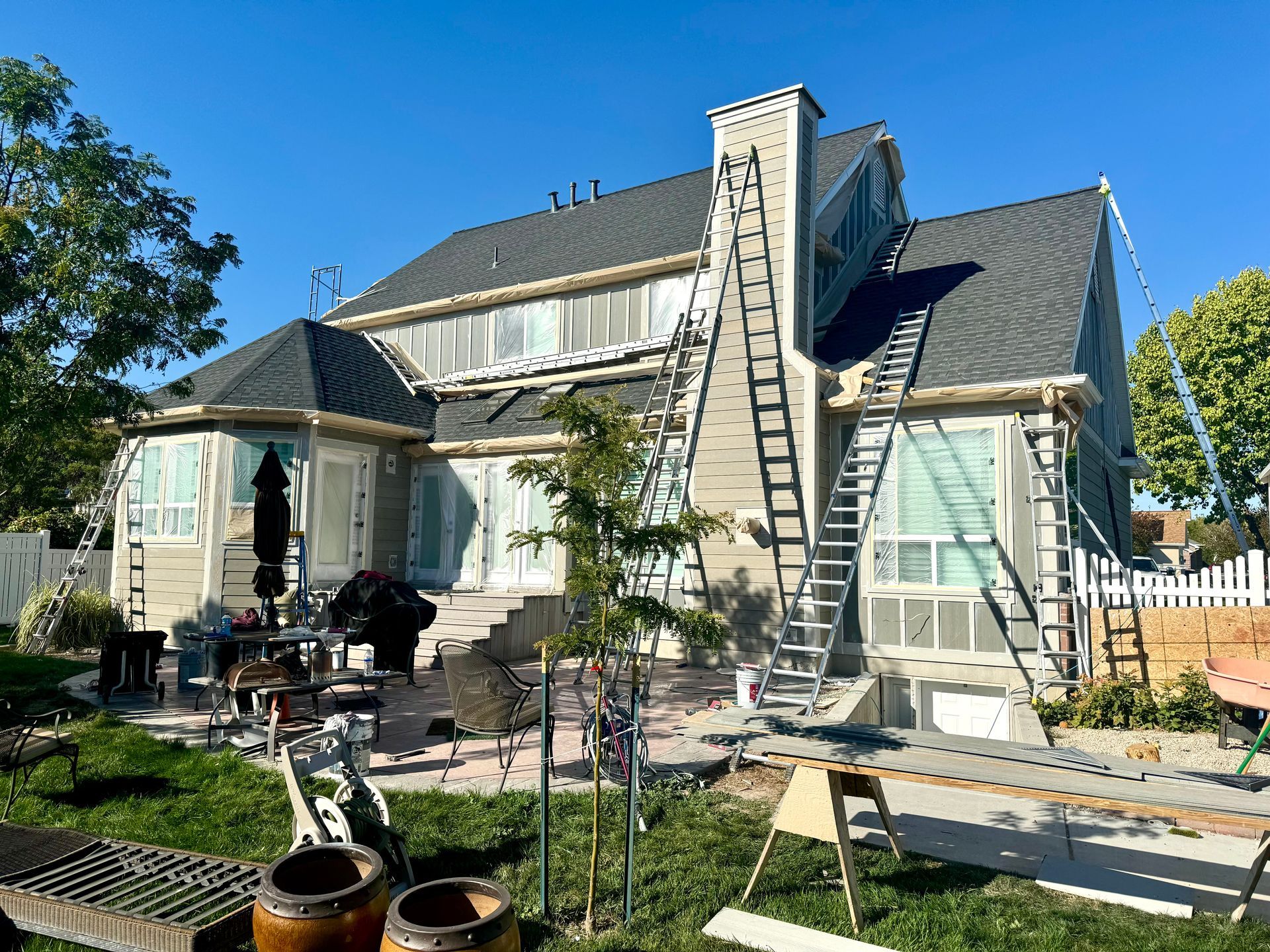 A large house is being painted with a ladder in the backyard.