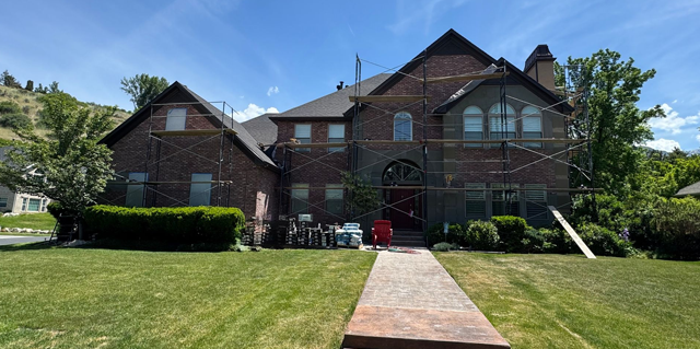 A large brick house with scaffolding around it is being painted.