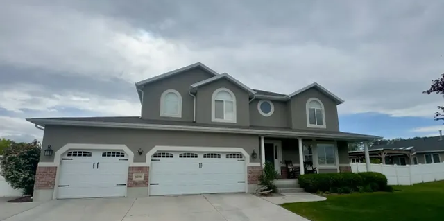 A large house with three garage doors is sitting on top of a lush green lawn.