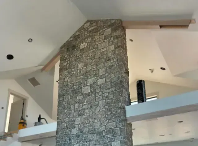 A living room with a stone fireplace and a ceiling fan